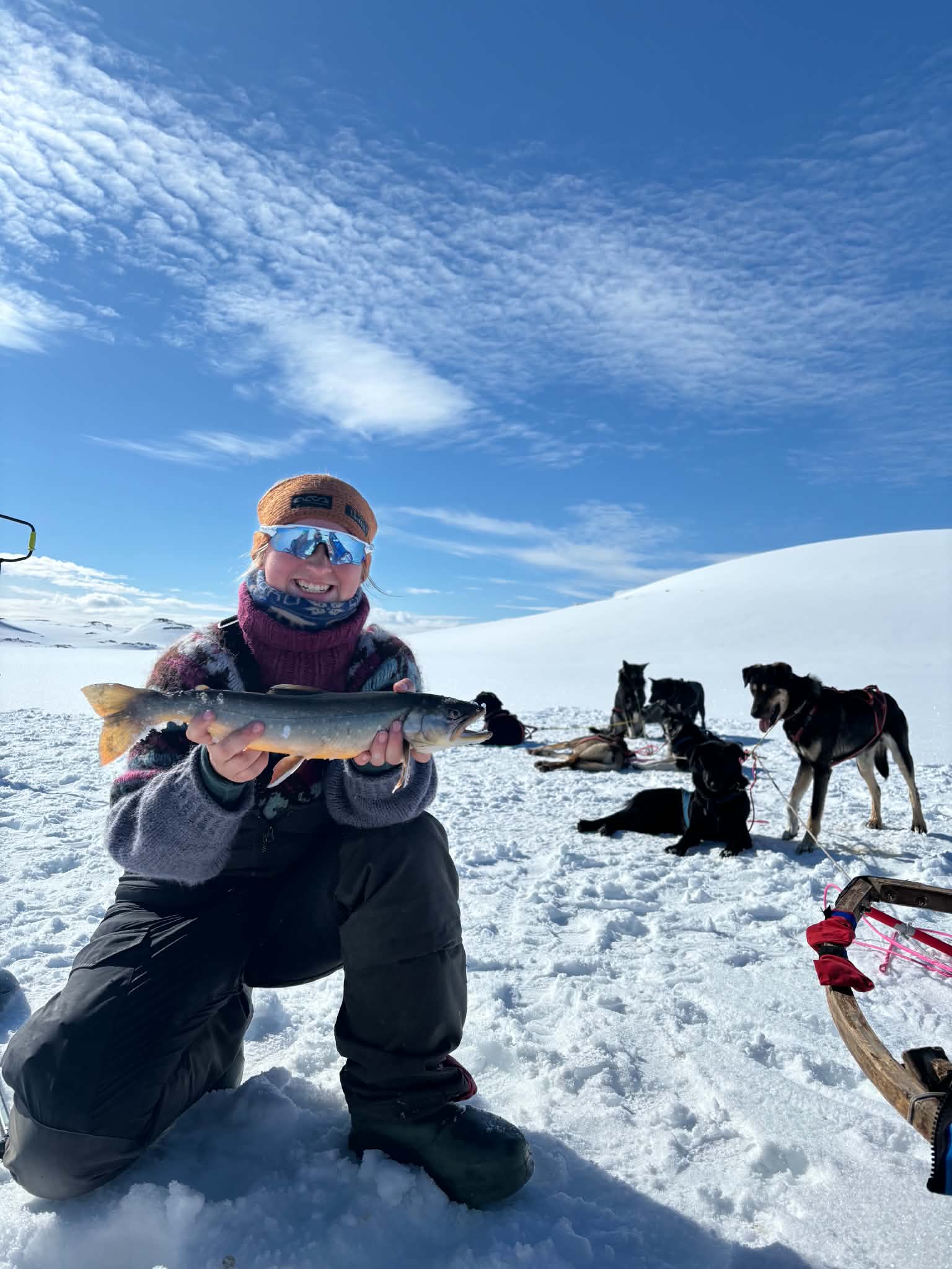 Guro Joten Søndmør holder en fisk på en vintertur med hundene i bakgrunnen