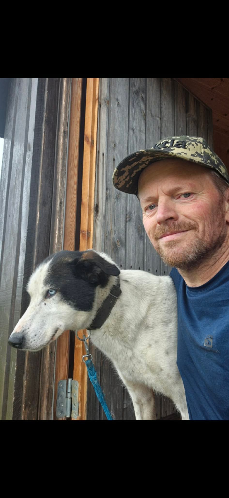 Jan Erik sitter ved siden av en svart-hvit hund utenfor en trebygning